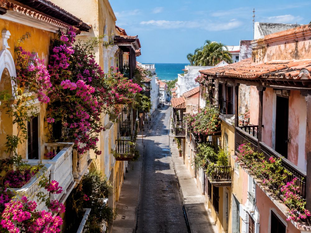 Balconies heavy with bougainvillea in Cartagena's walled Old City, the Caribbean visible at the end of the street